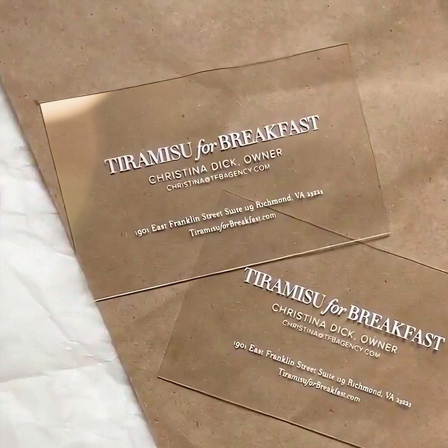 Two Clear business cards with white branding on a marble surface.