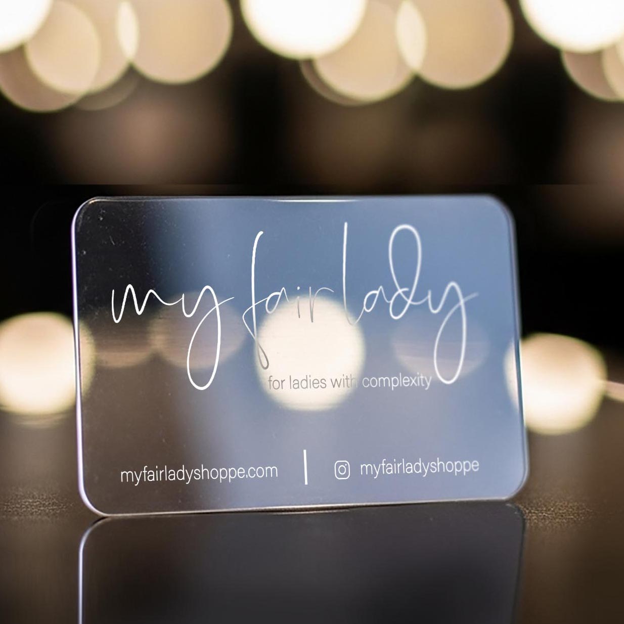 Clear Business Card with white branding against a blurred lights background