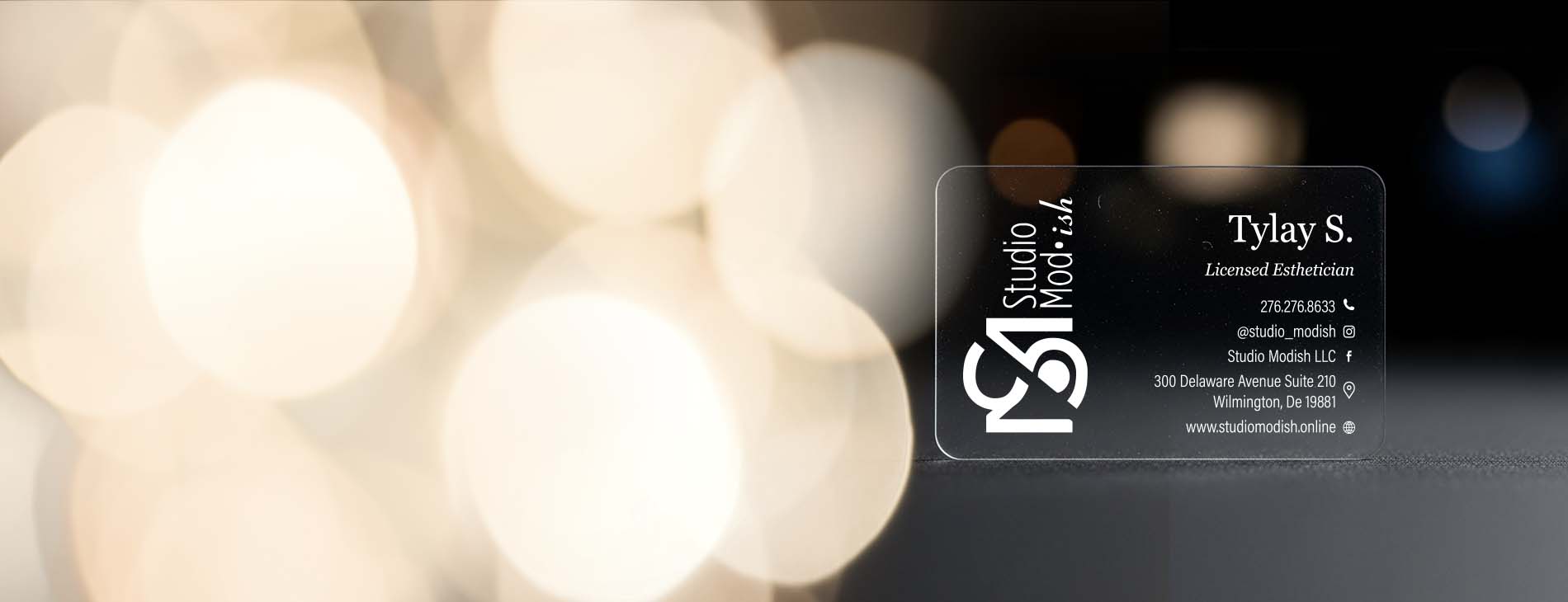 Clear business card with white branding on a blurred lights background