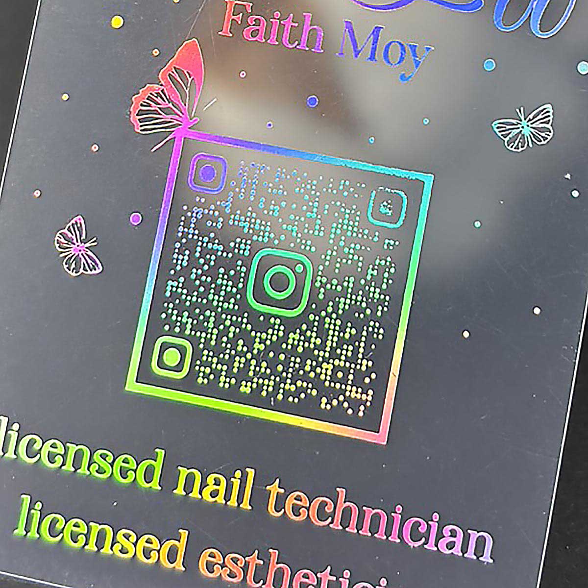 Holographic card with QR code and text about a licensed nail technician and esthetician, featuring butterflies.