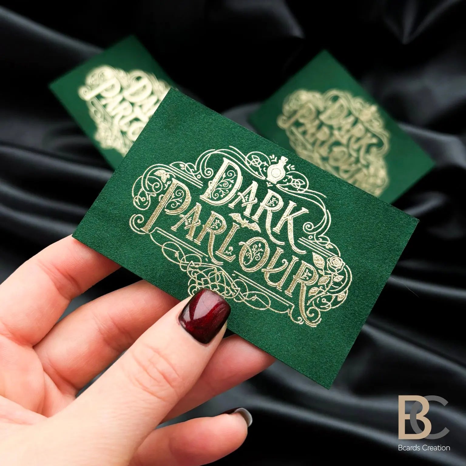 Hand holding a custom forest green velvet card with gold foil to showcase the professional 90x50 mm size and tactile finish