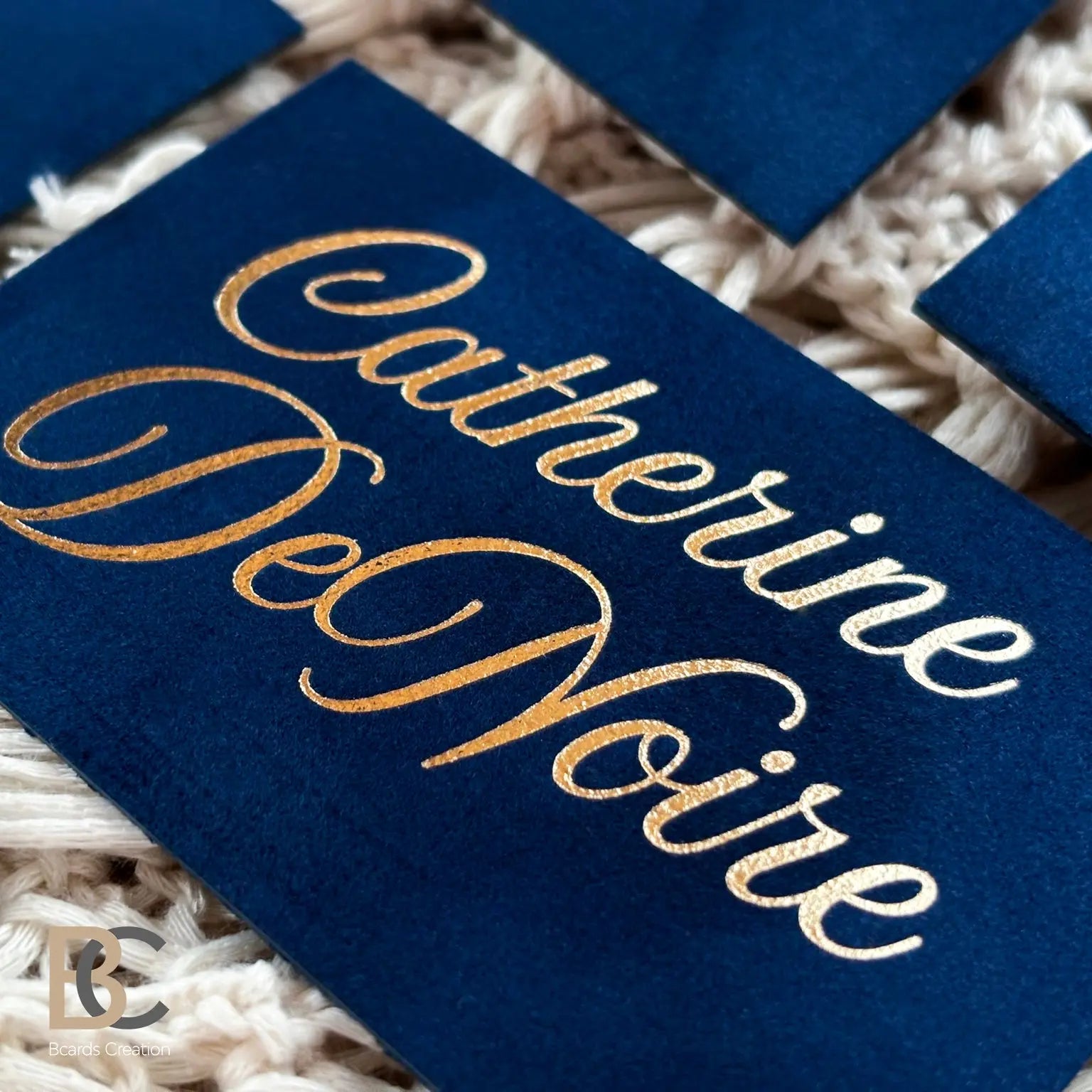 Macro shot of metallic gold foil on navy blue flocked texture. Highlights the physical lint surface and crisp debossing.